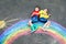 Two school kids boys with rainbow painted with colorful chalks on ground during pandemic coronavirus quarantine