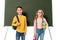 Two schoolchildren with backpacks and books standing near blackboard isolated on white.