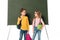 Two schoolchildren with backpacks and books standing near blackboard isolated on white.