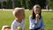 Two of schoolchildren are sitting in the park on the grass and eating an apple.