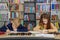 Two schoolchildren write and draw sitting at table in library. Classmates study in classroom