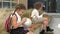 Two schoolgirls of different ages are sitting on a bench in the school yard. Little girl plays with a globe, the eldest