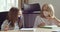 Two schoolgirls in medical protective masks sitting together at table at home at school classroom, looking at laptop