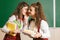 Two schoolgirls in school stand in a classroom with books. schoolgirl whispers in her friend`s ear a secret or gossip