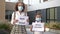 Two schoolgirls wearing medical masks with placards stand in front of the school building. The poster in the hands of a