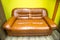 A two-seater faux leather sofa with brown armrests against a yellow wall. Interior furniture living