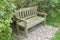 Two seater park bench set on gravel with hedgerow behind