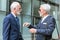 Two senior businessmen with gray hair and beard meeting and discussing in front of an office building. View from the side. Active