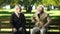 Two senior people laughing remembering young years sitting on bench in park