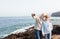 Two senior people take a selfie on the cliff of the ocean.Hugging and smiling. Morning soon outdoor with clear sky. Vacation and