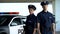 Two serious policemen in uniform and service cap posing near patrol car, order