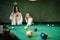 Two sexy girls in white bathrobe and swimsuit play pool billiards