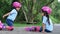 Two sibling sisters wearing protection pads and safety helmet practicing to roller skate on the street in the park. Active outdoor