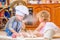 Two siblings - boy and girl - in chef`s hats sitting on the kitchen floor soiled with flour, playing with food, making mess and ha