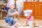 Two siblings - boy and girl - in chef`s hats sitting on the kitchen floor soiled with flour, playing with food, making mess and ha