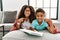 Two siblings lying on the sofa reading a book looking confident with smile on face, pointing oneself with fingers proud and happy