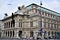 Two sides of a historic and important palace in Vienna. On the street, bicycle tourists and various pedestrians.