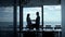Two silhouettes shaking hands in modern hall. Business partners leaving office