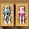Two silver and pink humanoid robots in boxes