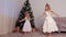 Two sisters children girls beautiful white dresses dancing near Christmas tree.