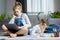 Two sisters lying on the floor at living room using laptop, playing and drawing