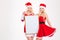 Two sisters in santa claus costumes posing with blank board