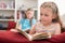 Two Sisters Sitting On Sofa At Home Reading Books Together