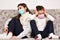 Two sisters sitting on the sofa with medical protective face masks