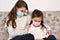 Two sisters sitting on the sofa with medical protective face masks