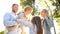 Two sisters and their parents have fun outdoor. Big young family in the park for a walk in the rays of sunlight