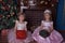 Two sisters in white with pink dress sitting with gifts in hands