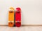 Two skateboards yellow and red stand upright against a wall on a wooden floor.