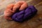 Two skeins of richly colored yarn on orange and deep purple, knitting and crochet, old wooden table top background