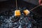 On two skewers, large pieces of marshmallow toasted over smoldering charcoal with the last sparks of fire and smoke. Small depth