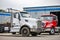 Two skid-mounted big rigs day cab semi trucks for transporting waste containers are parked in a warehouse awaiting another order