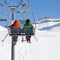 Two skiers on chair-lift and snowy ski slope