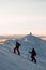 two skiers climb up to the top of a snowy mountain slope