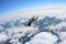 Two skydivers in color suits are falling above white clouds.