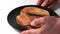 Two slices of fried bread made from white wheat flour are in a black round plate, hands are putting food