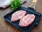 Two slices of raw pork neck fat slabs in a square cast iron grill pan on the table