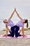 Two slim european sportswomen wearing equal the same activewear doing acro tandem yoga on mat on coast near the sea in the morning