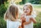 Two small angry girl friends or sister outdoors in sunny summer nature, pulling hair.