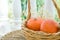 Two Small Bright Orange Heirloom Red Kuri Pumpkins in Wicker Basket Dry Autumn Plants on Rattan Table on Cottage Terrace. Fal