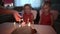 Two small charming and dressed twin sisters gathered near the festive cake with burning candles. Birthday in the family.