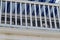 Two small dogs looking through a white fence on a porch down to the street below