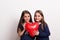 Two small girls in a studio, holding a red heart balloon in front of them.