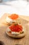 Two small starters blinis with sour cream and salted salmon red caviar served on mango tree wooden board