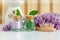 Two small vintage glass bottles with purple and green bath salts foot soak, wooden hair brush and lilac flowers. Copy space