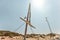 Two small wind turbines, one of them broken, standing on desert, strong back light sun in background