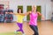 Two smiling athletic women doing aerobic dancing exercises holding their arms sideward indoors in fitness center.